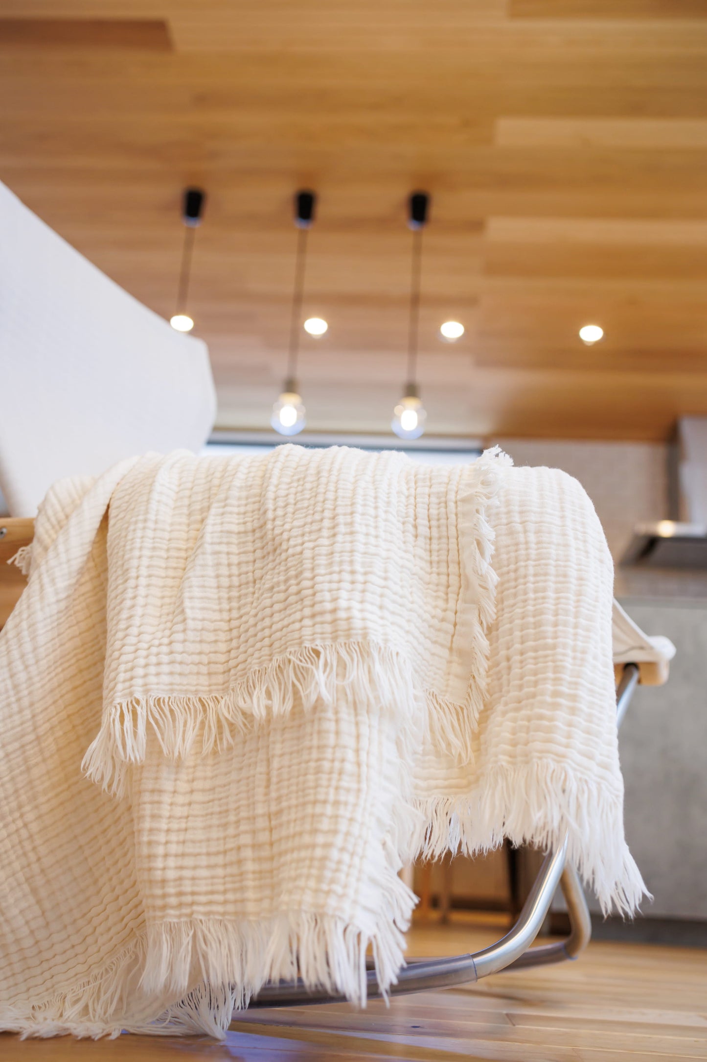 Undyed 4-layer crinkle gauze muslin baby blanket with fringed edges, shown as a soft throw-style lifestyle photo