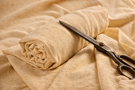 Rolled undyed cotton-linen fabric with scissors, highlighting natural texture and stitch-ready fabric for sewing and dyeing