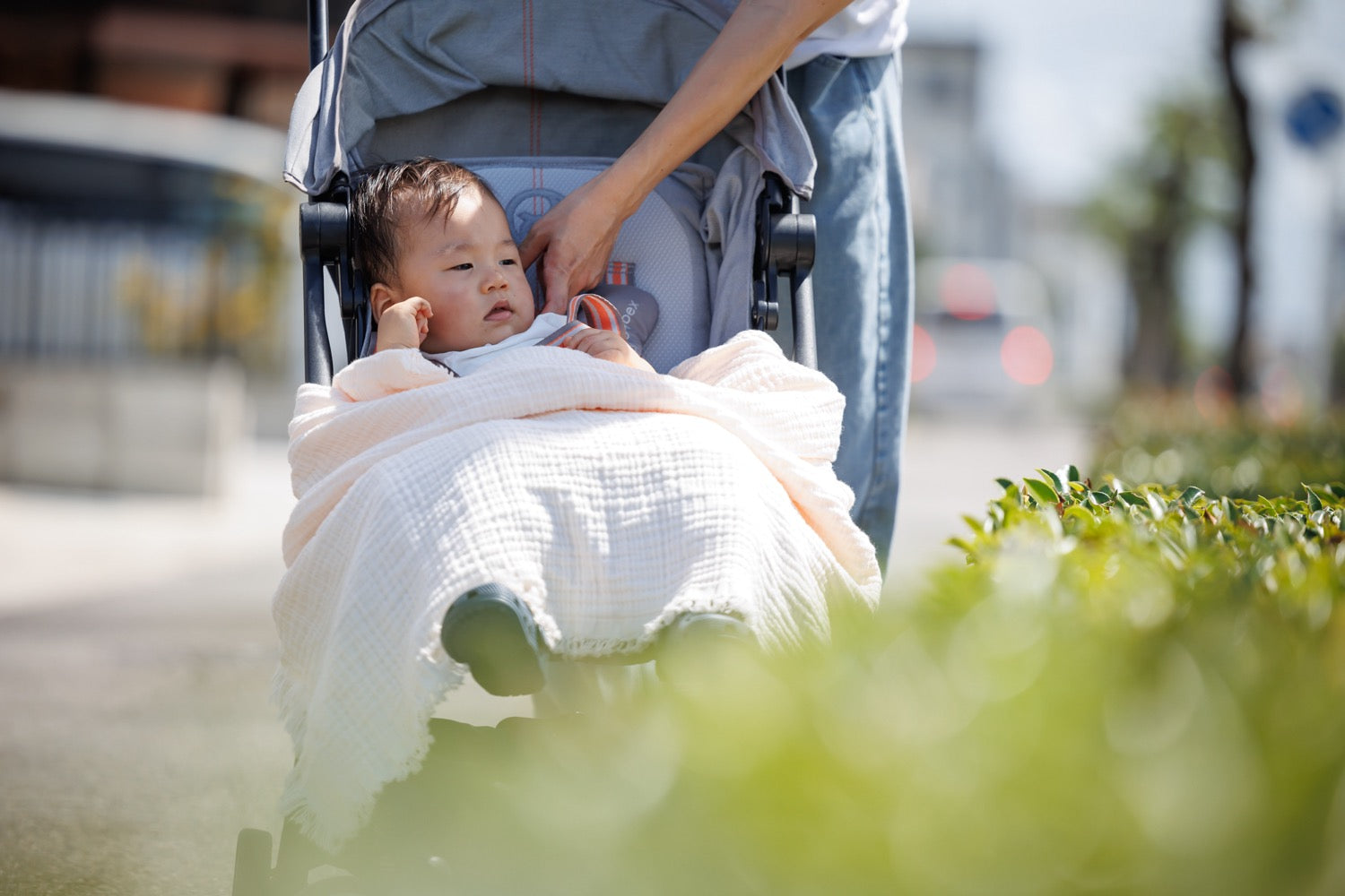 A baby enjoys a comfortable ride in a stroller with a crinkle blanket draped over.